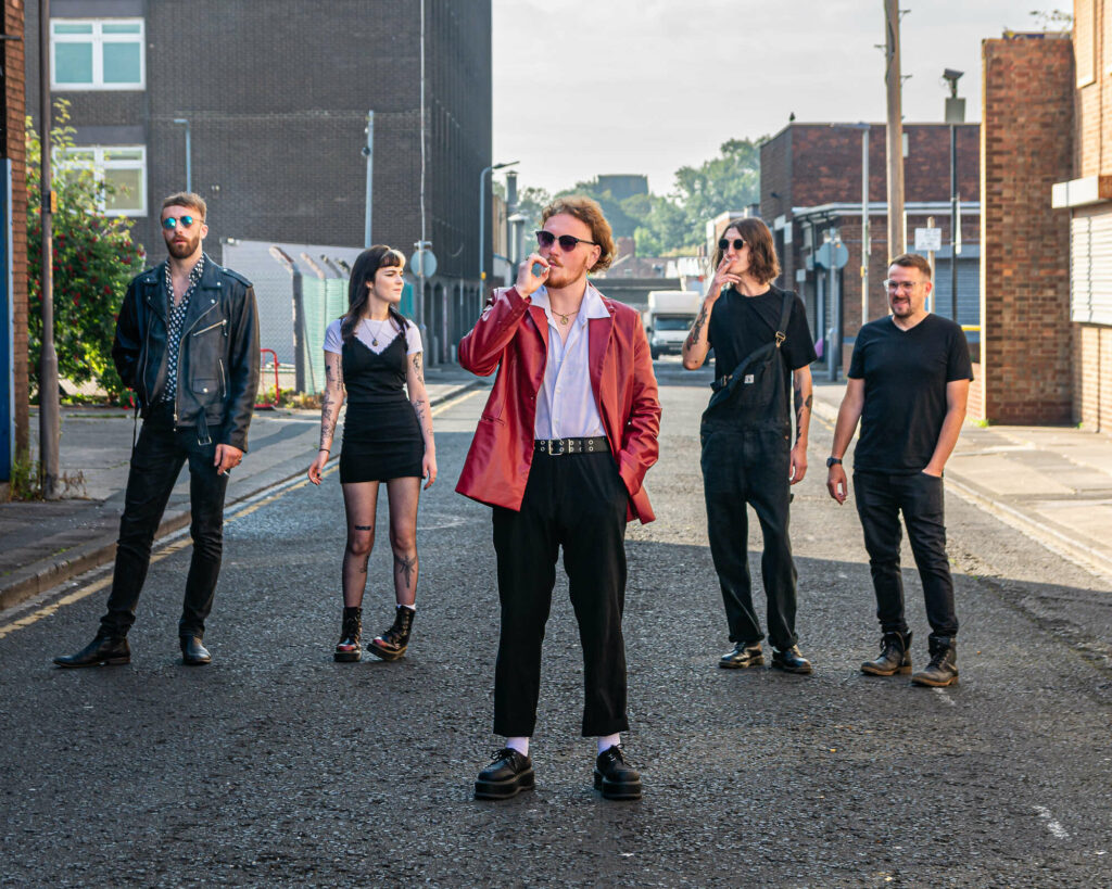 5 piece group Dossers stand in an alley way, the front person is smoking