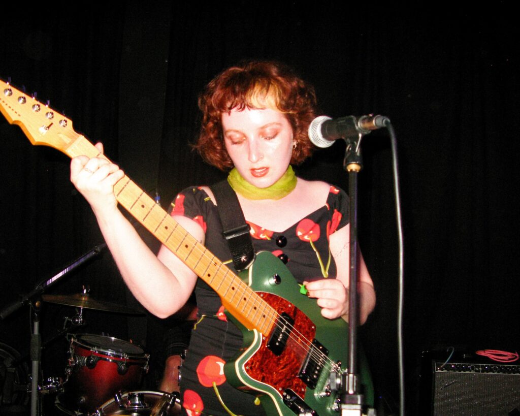 Tina Sandwich plays guitar in front of a microphone